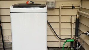 A white portable heater on a yellow base outside a house with beige siding.