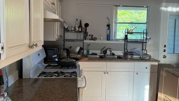 A kitchen with white cabinets, a granite countertop, a stove, and a window with a view of greenery.