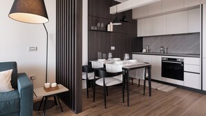 Une cuisine moderne avec des armoires blanches, un comptoir noir et un four encastré. On y trouve également un coin repas avec une table pour deux personnes, des chaises et une lampe.