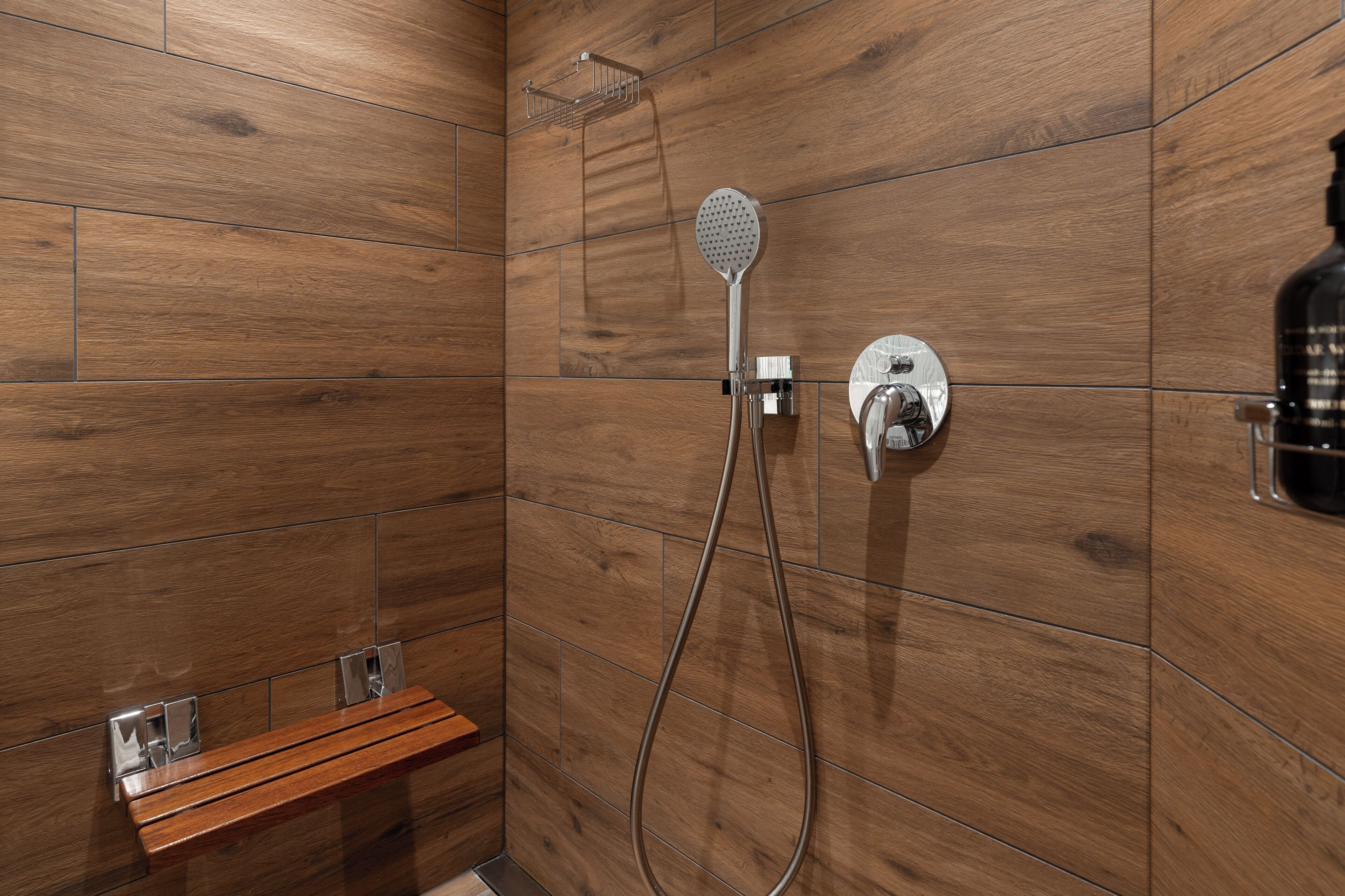 Un espace douche avec un revêtement mural en bois, une douchette à main et un panneau de commande fixé au mur.