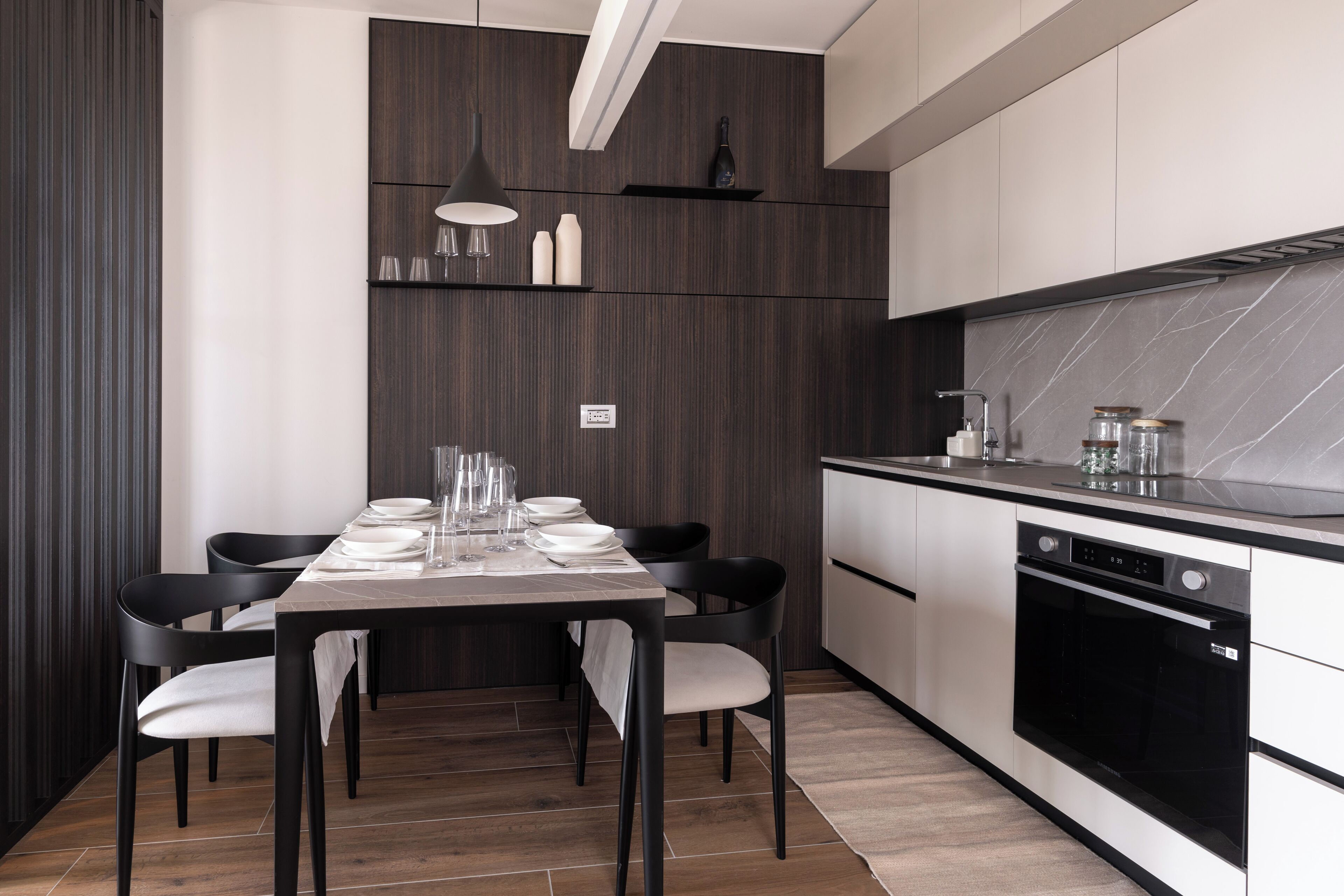 Een moderne keuken met een eethoek, met een wand van donker hout, witte kasten en een zwarte oven.