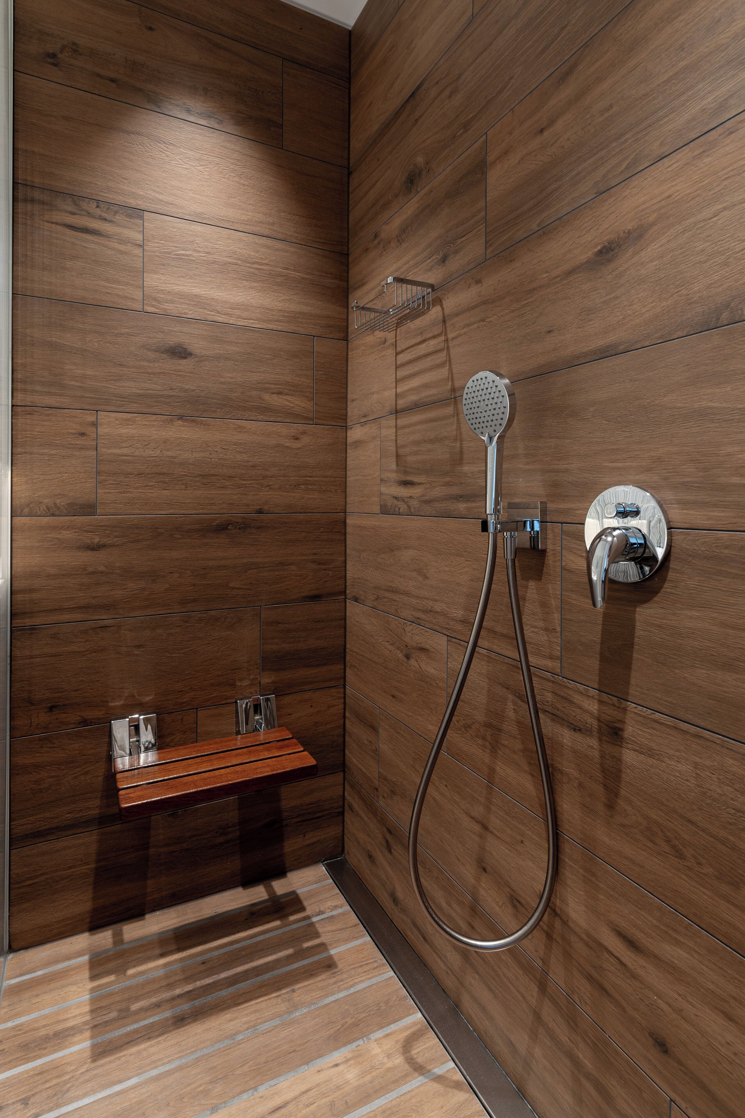 Un espace douche moderne avec un revêtement mural en bois, une douchette à main et un panneau de commande fixé au mur.