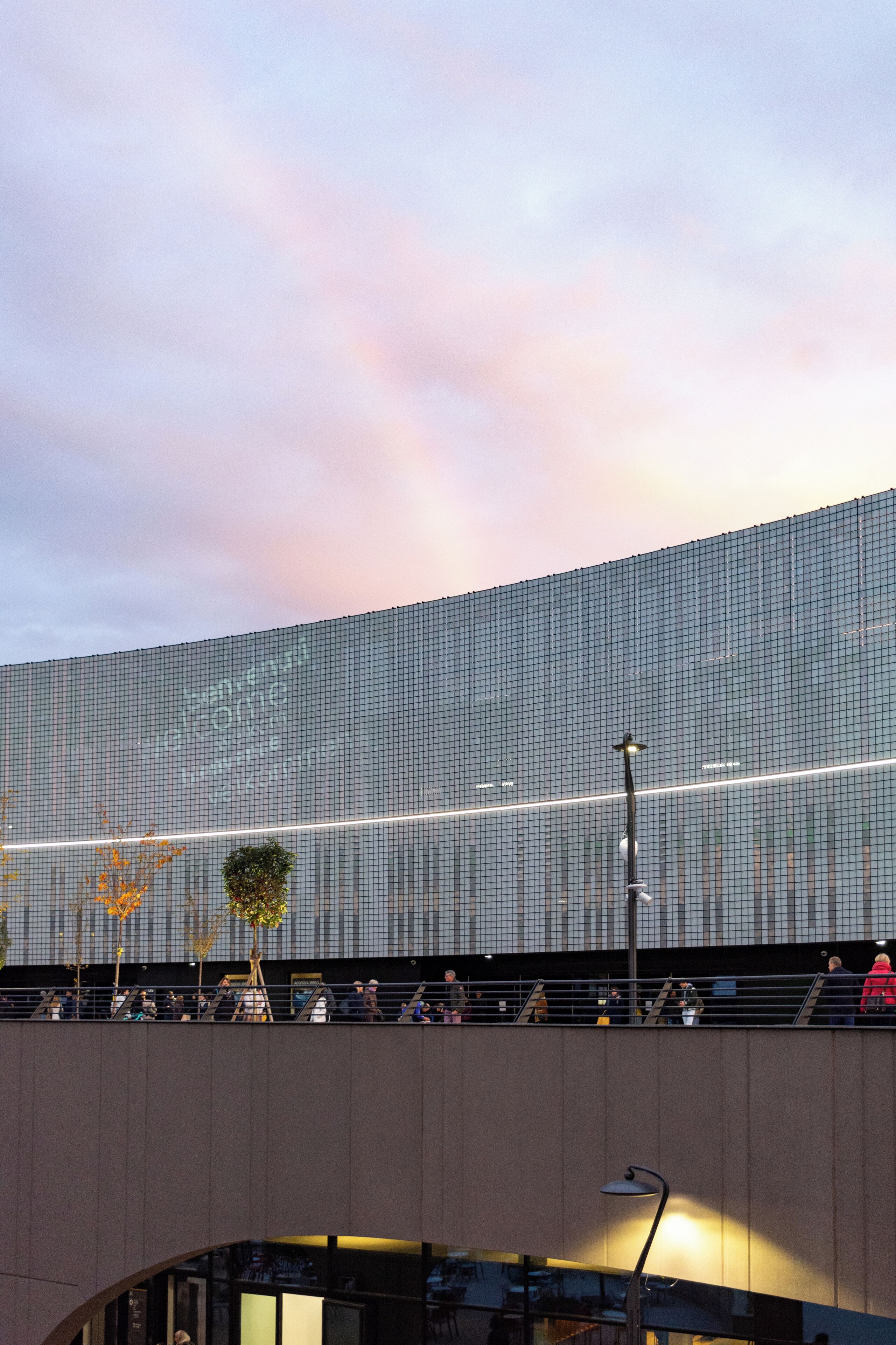 A modern building with a curved facade and a covered walkway with seating.