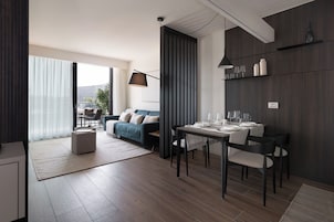 Un soggiorno moderno con zona pranzo, con un divano, un tavolo da pranzo per quattro persone e un'ampia finestra.