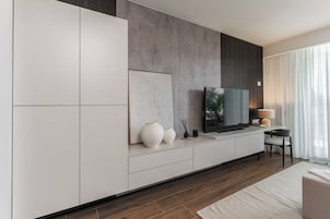 Un soggiorno moderno con una grande televisione a schermo piatto, un tavolino consolle minimalista e un'ampia finestra con tende leggere.