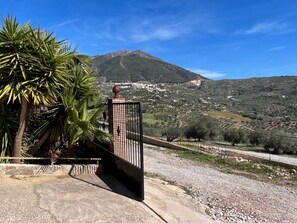 Una entrada con reja que ofrece vistas a un paisaje montañoso y un pueblo al fondo.