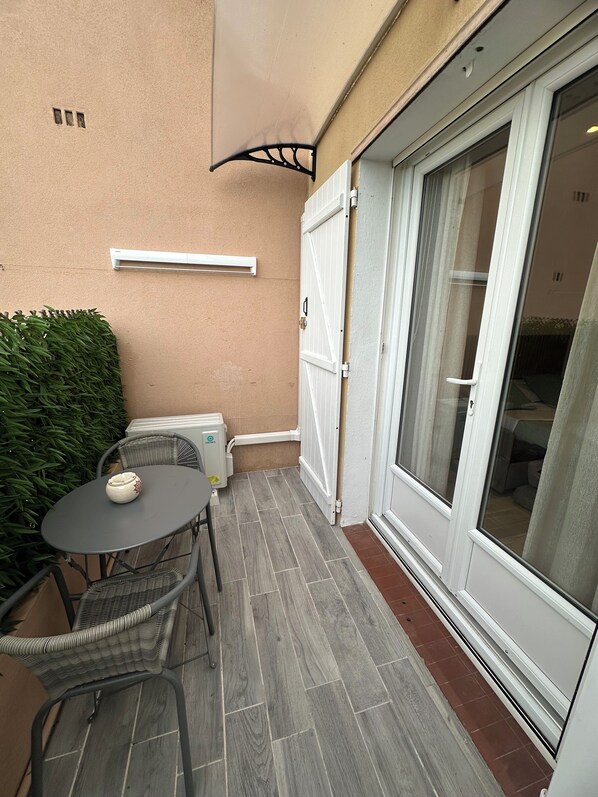 Ein kleiner Patio-Bereich mit Tisch und Stühlen, einem Blumentopf und einer Glastür zum Innenraum.
