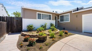 A residential backyard with a paved patio, a wooden fence, and a variety of potted plants and flowers.