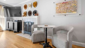A modern living room with a fireplace, grey armchairs, a round table, and a wall-mounted map.