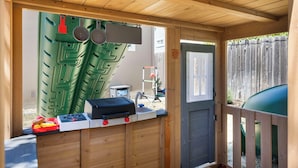 A wooden playhouse with a counter, a sink, and a door.