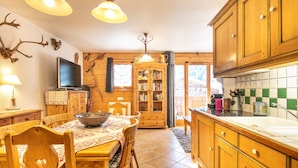 A wooden interior with a dining table, chairs, a television, cabinets, and a kitchen area. - Les Préséloignés Apartment with Mountain View (Pralognan-la-Vanoise)