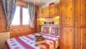 A wooden cabin room with a bed, curtains, a hanging light fixture, and wooden cabinets. - Les Préséloignés Apartment with Mountain View (Pralognan-la-Vanoise)