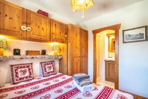 Une chambre avec des armoires en bois, un lit avec une literie à motifs et une table de chevet avec une lampe.