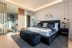 A modern bedroom with a large bed, a bedside table, a hanging light fixture, and a potted plant.