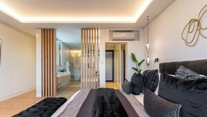 A modern bedroom with a large bed, a dark-colored sofa, and a decorative wall piece. - Walk to beach, Pool, Camps Bay -Terrace Royale Apt (Cape Town)