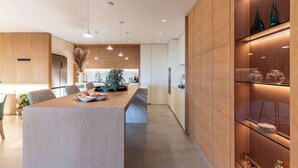 A modern kitchen with a central island, pendant lighting, and wooden cabinetry. - Walk to beach, Pool, Camps Bay -Terrace Royale Apt (Cape Town)