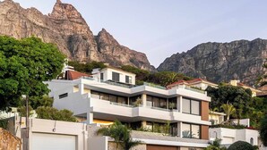 A modern multi-story residential building with balconies, a garage, and a stone wall. - Walk to beach, Pool, Camps Bay -Terrace Royale Apt (Cape Town)