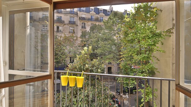 Ein Balkon mit gelben Eimern und Blick auf Pariser Gebäude.