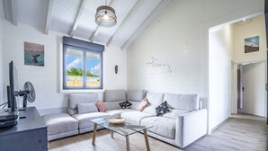 A modern living room with a grey sectional sofa, a glass coffee table, and a large window with a view of greenery.