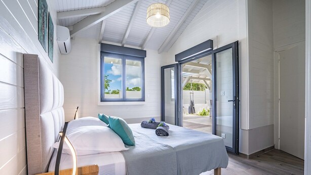 A bedroom with a bed, bedside table, and a window with a view of the outdoors.