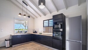 A modern kitchen with dark cabinetry, stainless steel appliances, and a large window providing natural light.
