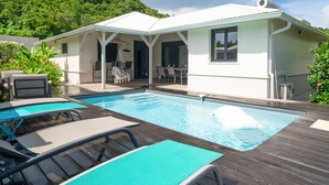 A poolside area with a covered patio, lounge chairs, and a view of a house with a white exterior and a covered deck.