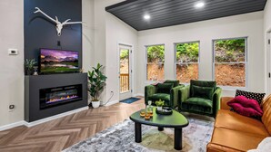 A modern living room with a fireplace, a mounted TV, and a large window with a view of greenery.