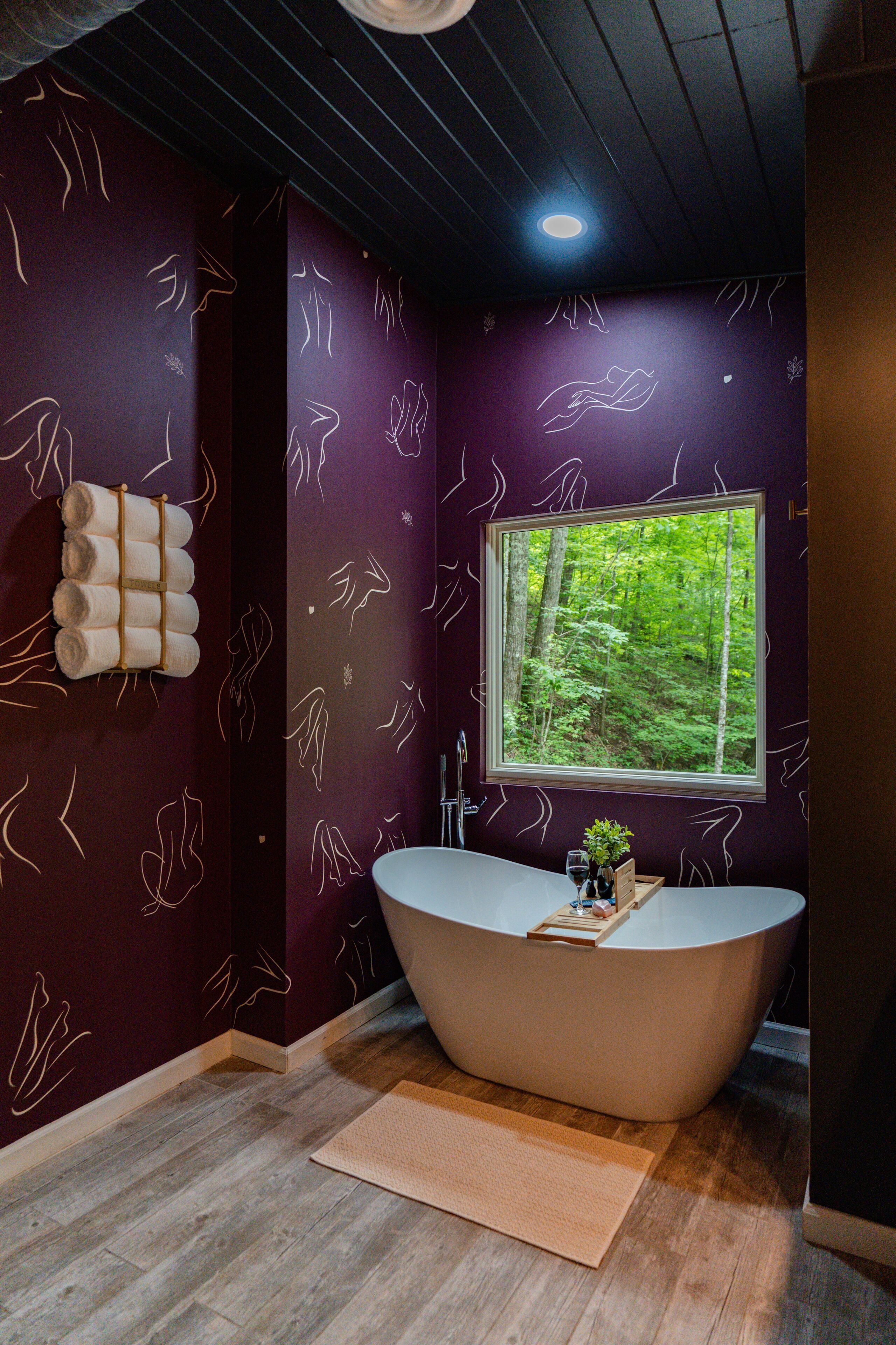 Een moderne badkamer met een vrijstaand bad, een raam met uitzicht op een bos, en een wand met abstracte lijnpatronen.