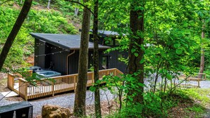 A cabin with a hot tub, wooden deck, and a view of the forest.