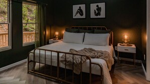 A bedroom with a bed, bedside tables, and a view of the outdoors.