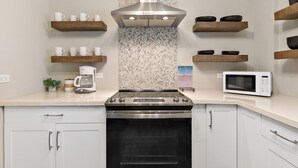 Una cocina moderna con armarios blancos, electrodomésticos de acero inoxidable, estantes de madera y salpicadero con diseño.