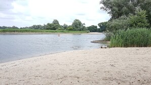 A sandy beach with a calm river, dense greenery, and trees in the background. - Holiday Apartment Havelnixe with Private Terrace and Wi-Fi (Bahnitz)