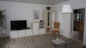 A living room with a television, a cabinet, a wicker chair, a glass table, and a hanging light fixture. - Holiday Apartment Havelnixe with Private Terrace and Wi-Fi (Bahnitz)