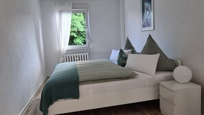 A bedroom with a bed, a bedside table, a window with curtains, and a wall-mounted picture. - Holiday Apartment Havelnixe with Private Terrace and Wi-Fi (Bahnitz)