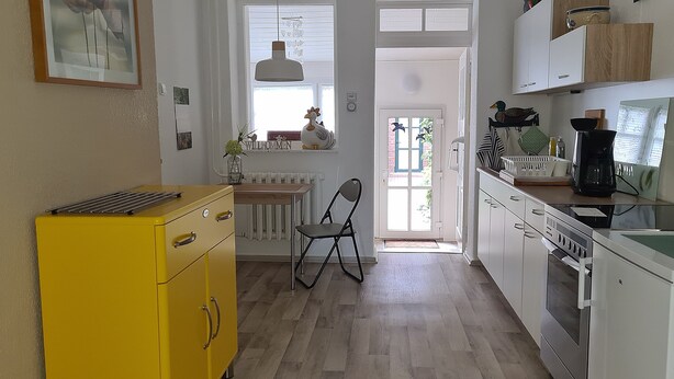A kitchen with a yellow cabinet, a chair, a window, and a door leading outside. - Holiday Apartment Havelnixe with Private Terrace and Wi-Fi (Bahnitz)