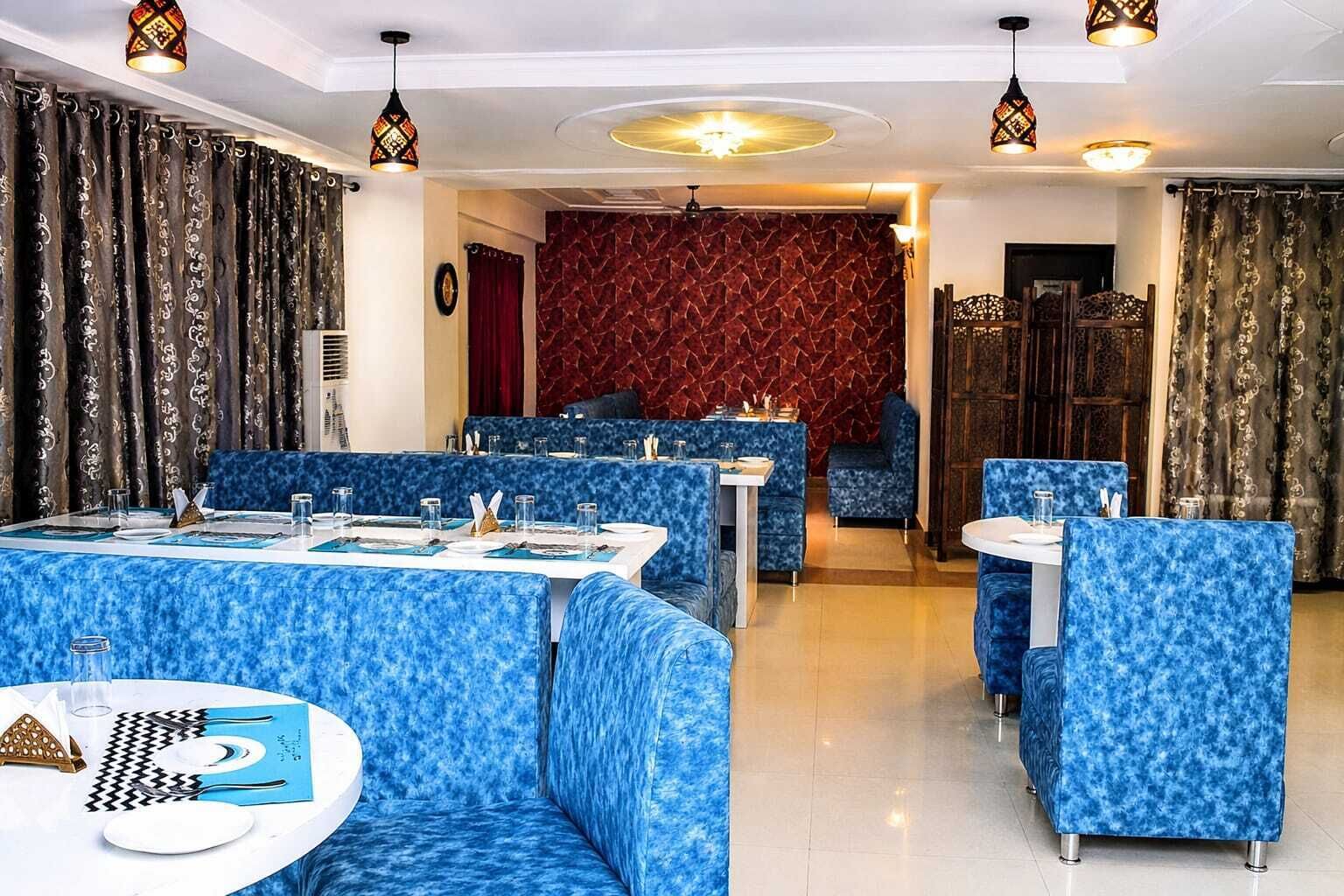 A restaurant with blue patterned booths and tables, red patterned wall, and hanging pendant lights.