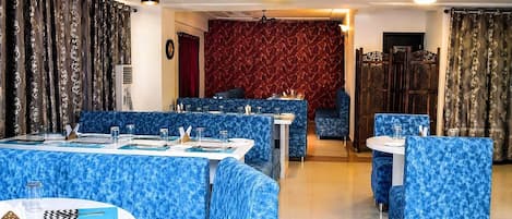 Un restaurante con asientos y mesas de color azul estampados, pared de color rojo con estampado e iluminación colgante.