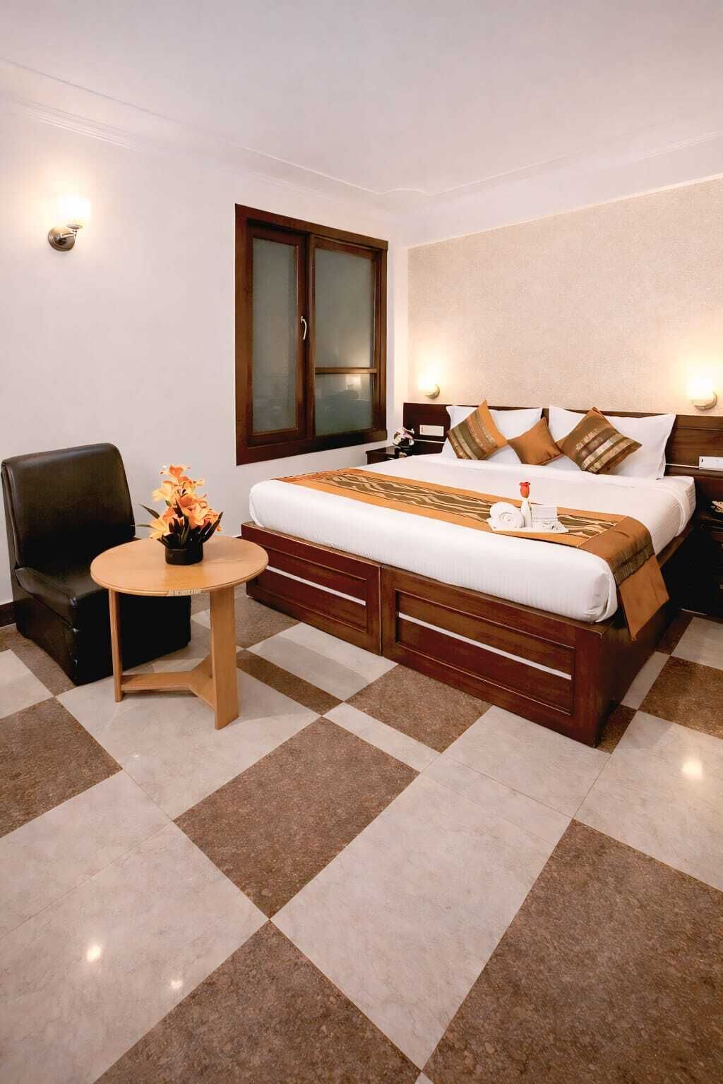 A hotel room with a bed, a chair, a small table, and a window.