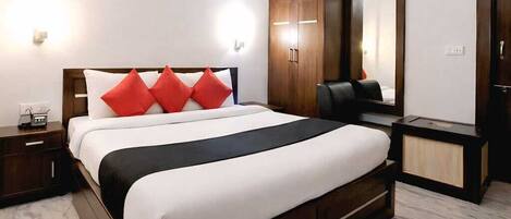 A modern hotel room with a large bed, a wooden wardrobe, a desk, and a mirror.