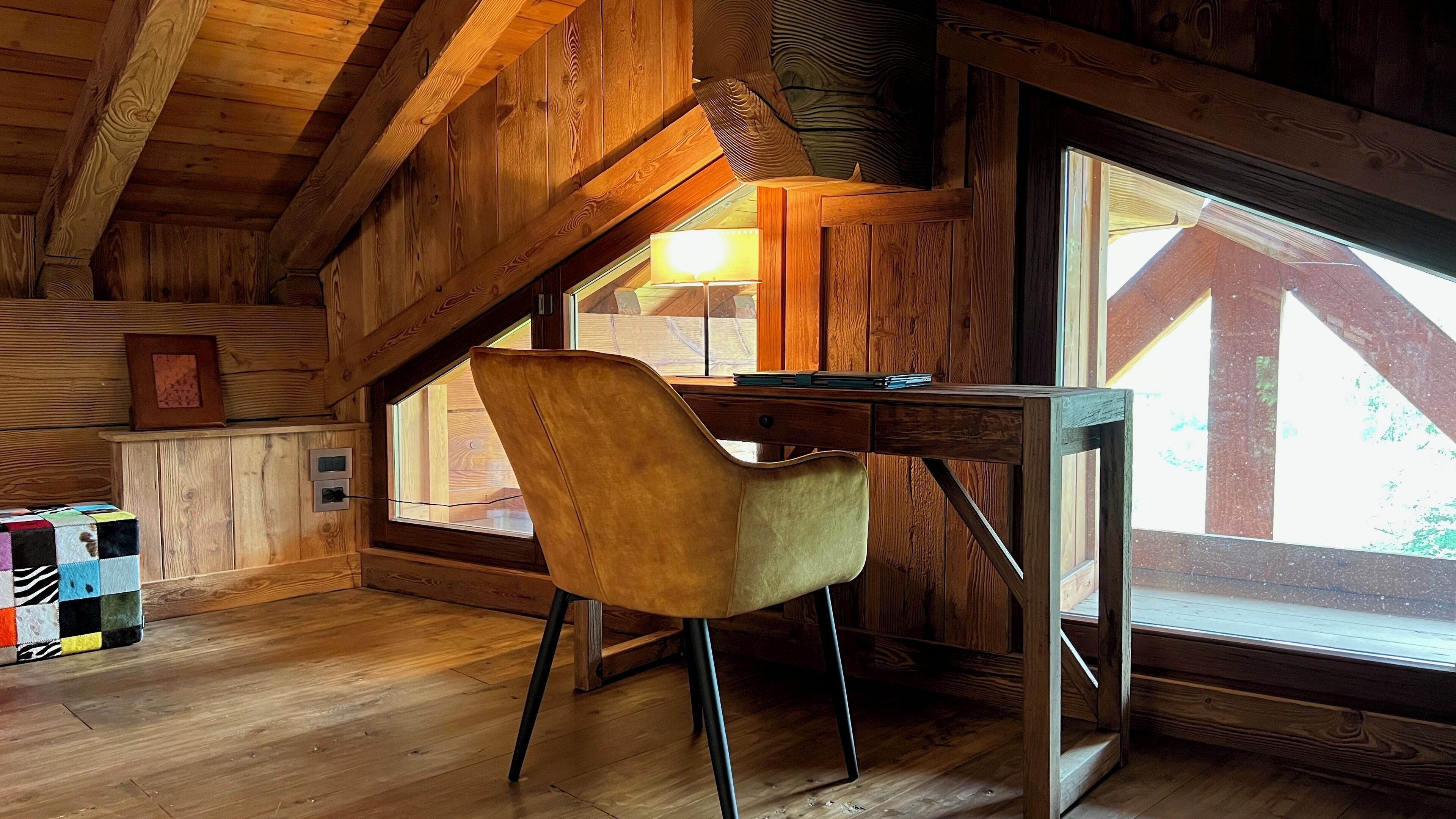 Ein Holzinterieur mit Schreibtisch und Stuhl, großen Fenstern und einer Holzbalkendecke.