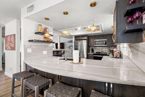 A modern kitchen with a curved island, stainless steel appliances, pendant lighting, and a seating area with stools. - Family Fun Resort Home! Heated Pool, Hot Tub, Pickleball & Arcades! 9 beds (Seminole)
