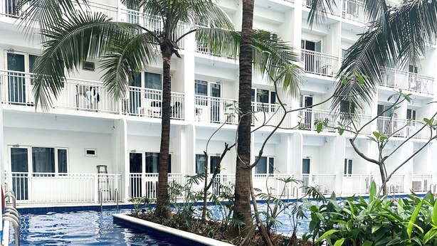 A swimming pool with a clear blue water pattern, surrounded by palm trees and a white building with balconies. - Crizzy's Hub Sariel @ Shore Residences (Pasay City, Metro Manila)