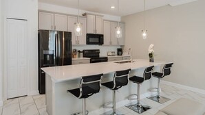 Una cocina moderna con armarios blancos, electrodomésticos de acero inoxidable y taburetes de bar.