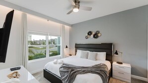 Habitación de hotel moderna con una cama grande, ventilador de techo, vista a la ciudad y un pequeño escritorio con lámpara.
