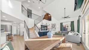 A spacious living area with a wooden dining table, a sofa, and a staircase leading to an upper level. - Heated Pool! MiniGolf! Hot Tub! Fire Pit! Lakefront! (Hot Springs)