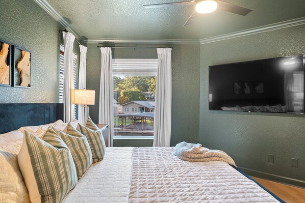 A bedroom with a bed, pillows, a TV, and a window with curtains. - Heated Pool! MiniGolf! Hot Tub! Fire Pit! Lakefront! (Hot Springs)