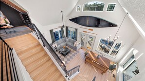A spacious living area with a modern staircase, a large window, and a dining area with a view of the outdoors. - Heated Pool! MiniGolf! Hot Tub! Fire Pit! Lakefront! (Hot Springs)