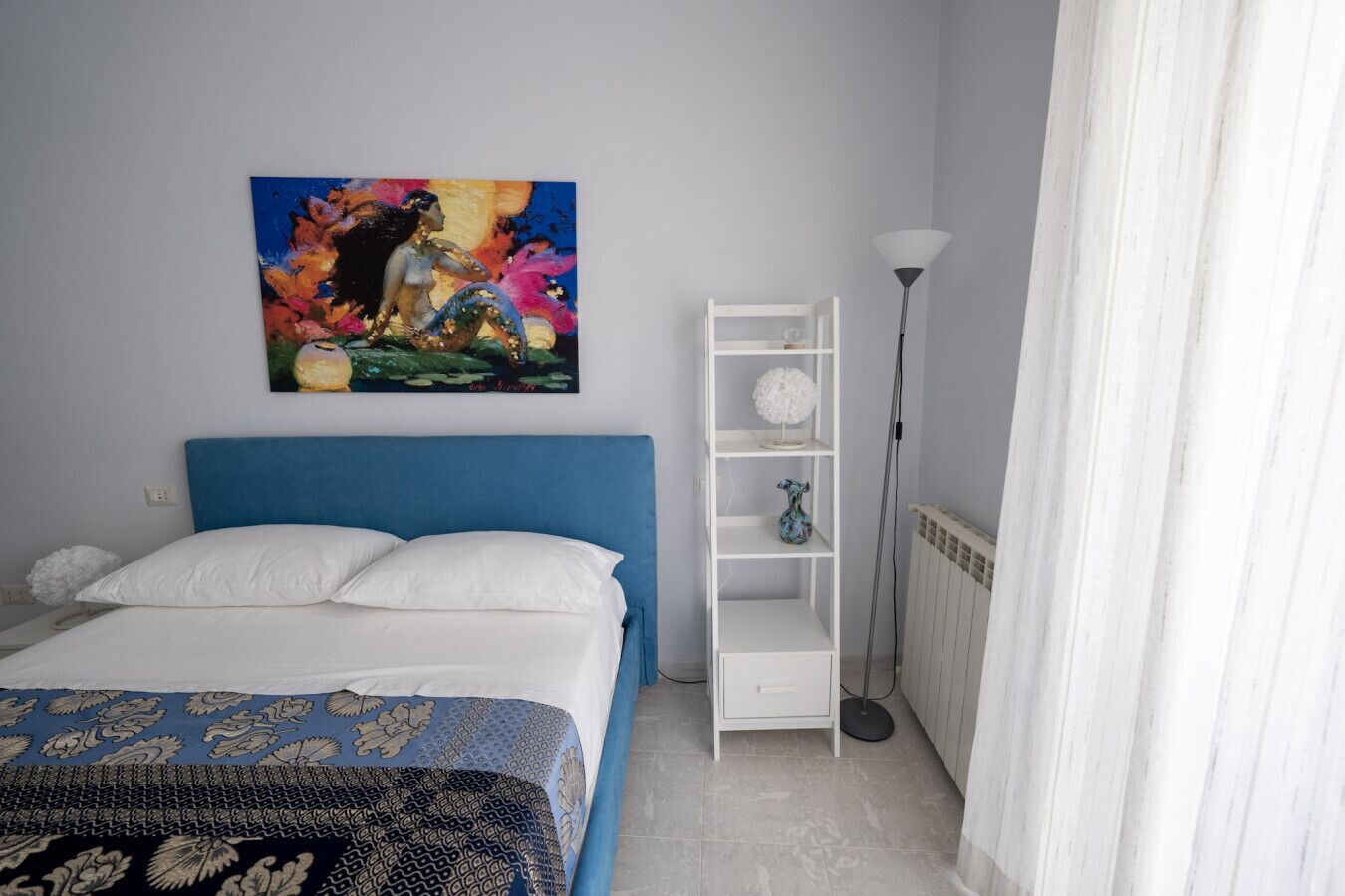 Un dormitorio con una cama, una estantería blanca, una lámpara de pie y un cuadro en la pared.