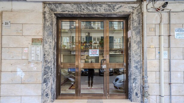 A building entrance with a marble facade, glass doors, and a sign indicating a business inside. - MARINELLI HOUSE - Song'Parthenope - Naples (Napoli)