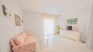 A modern living room with a sofa, a glass coffee table, a TV on a white cabinet, and a large window with curtains. - MARINELLI HOUSE - Song'Parthenope - Naples (Napoli)